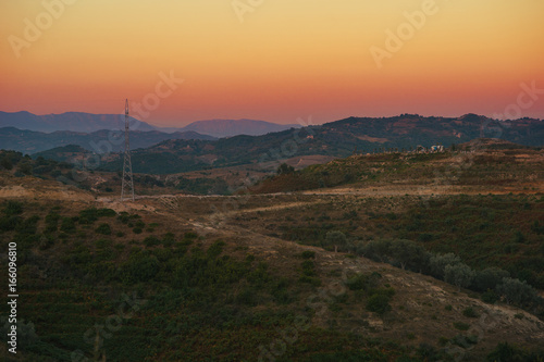 Evening panorama of a countryside between Tirana and Durres, Albania. Hills and forests captured during scenic sunset with orange sky and mist. 