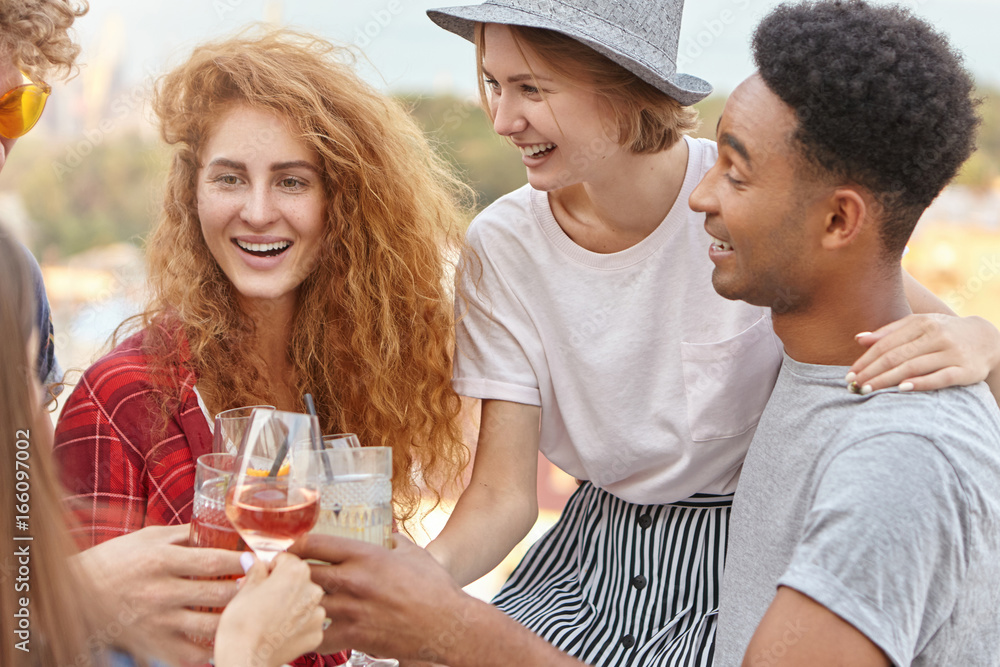 Group of mixed race friends raising drinks for cheers celebration, embracing each other, celebrating birthday of their friend. Happy youngsters clinking glasses with wine and cocktails, smiling Group of mixed race friends raising drinks for cheers celebration, embracing each other, celebrating birthday of their friend. Happy youngsters clinking glasses with wine and cocktails, smiling