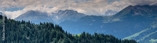 panoramic view of ridges of mountains in Switzerland with a small red cabin in a clearing in the foreground photo