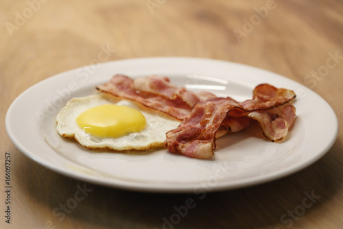 fried egg with crispy bacon stripes on plate