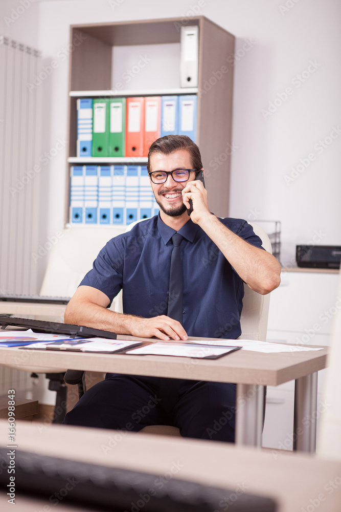 Smiling corporate worker in blue shirt and tie talking on the phone. Portrait of successful entrepreneur in his modern office. Happy young corporate worker at his job Smiling corporate worker in blue shirt and tie talking on the phone. Portrait of successful entrepreneur in his modern office. Happy young corporate worker at his job