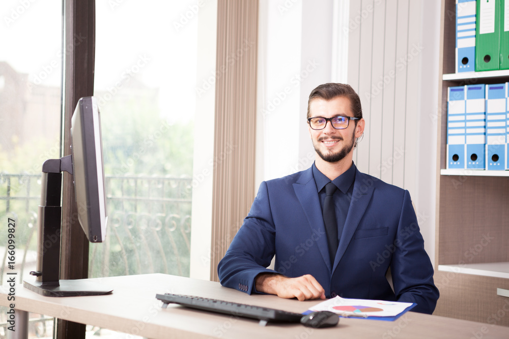 Businessman in suit working at his computer next to a glass window. Image of successful anc competitive entrepreneur at his work place Businessman in suit working at his computer next to a glass window. Image of successful anc competitive entrepreneur at his work place
