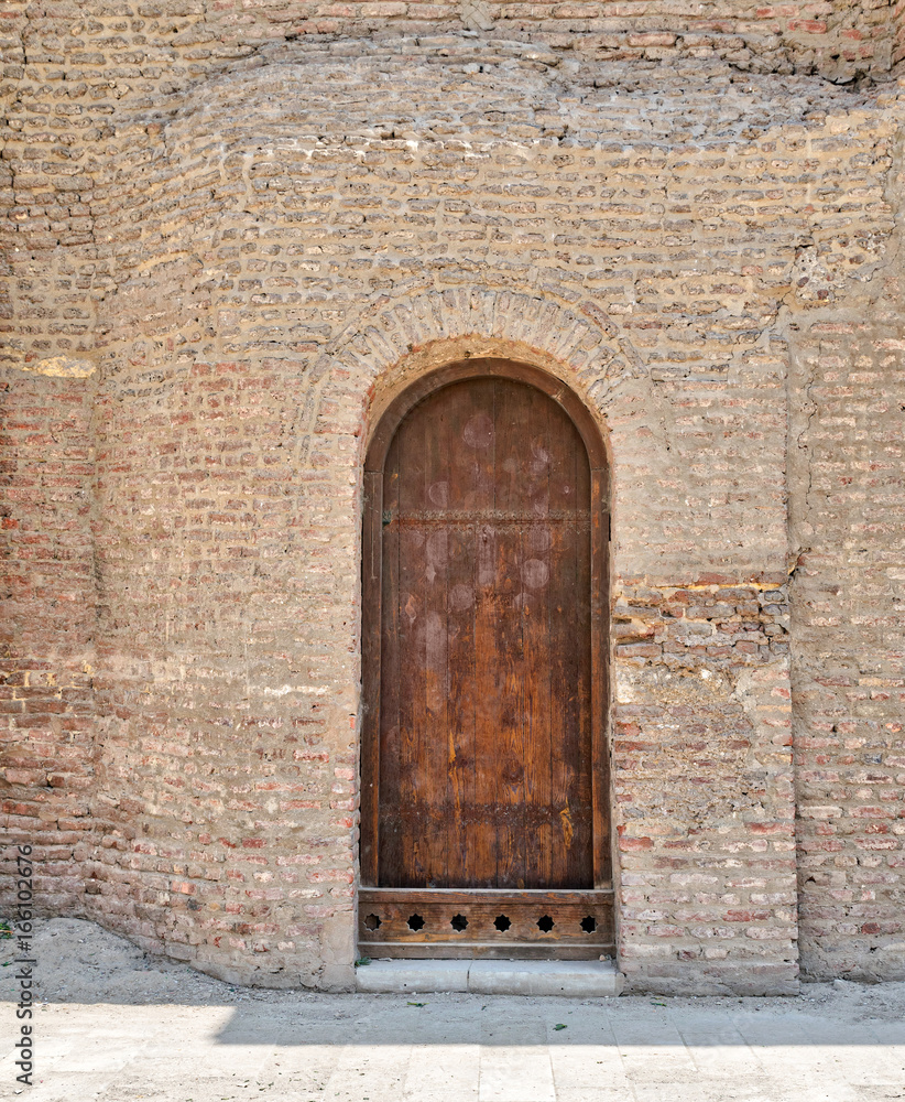 Grunge wooden aged vaulted door on exterior stone bricks wall of Amr Ibn Al-As, Medieval Cairo, Egypt Grunge wooden aged vaulted door on exterior stone bricks wall of Amr Ibn Al-As, Medieval Cairo, Egypt