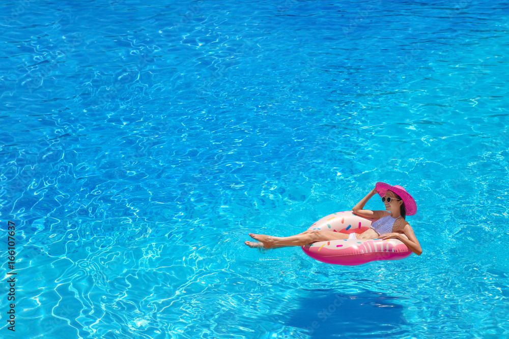 Beautiful young woman with inflatable donut in blue swimming pool