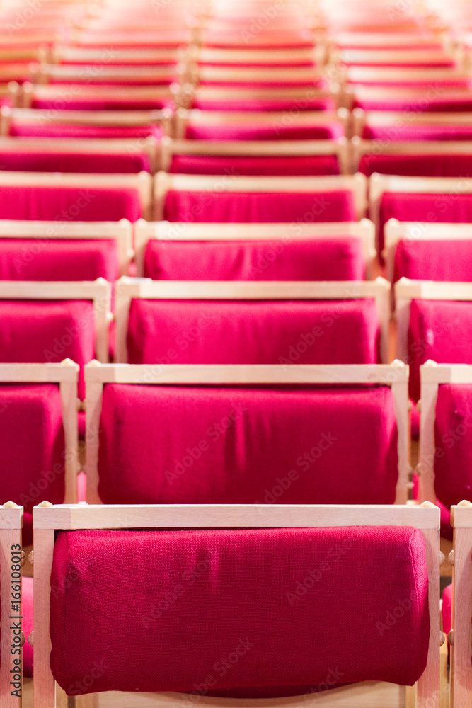 Fototapeta premium Rzędy pustych, czerwonych, aksamitnych siedzeń wewnątrz kościoła, stadionu, teatru czy sali koncertowej rozciągają się w dal i wypełniają kadr.