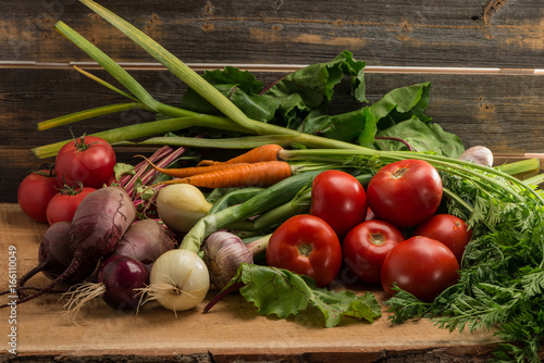 Green onions, garlic, carrots, beet and tomatoes against the background of old grey boards