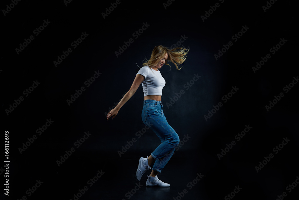 Full lenght studio shot of blonde European girl wearing crop top and blue stretch jeans stretching, doing aerobics or dancing. People, sports, fitness, dance, energy, flexibility and active lifestyle