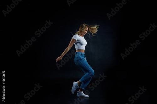 Full lenght studio shot of blonde European girl wearing crop top and blue stretch jeans stretching, doing aerobics or dancing. People, sports, fitness, dance, energy, flexibility and active lifestyle