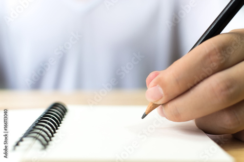 Hand of man with pencil writing on notebook