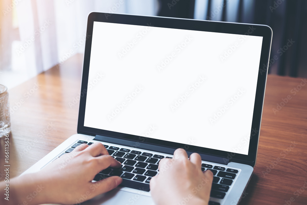 Mockup image of a woman using and typing on laptop with blank white screen on wooden table in modern cafe Mockup image of a woman using and typing on laptop with blank white screen on wooden table in modern cafe