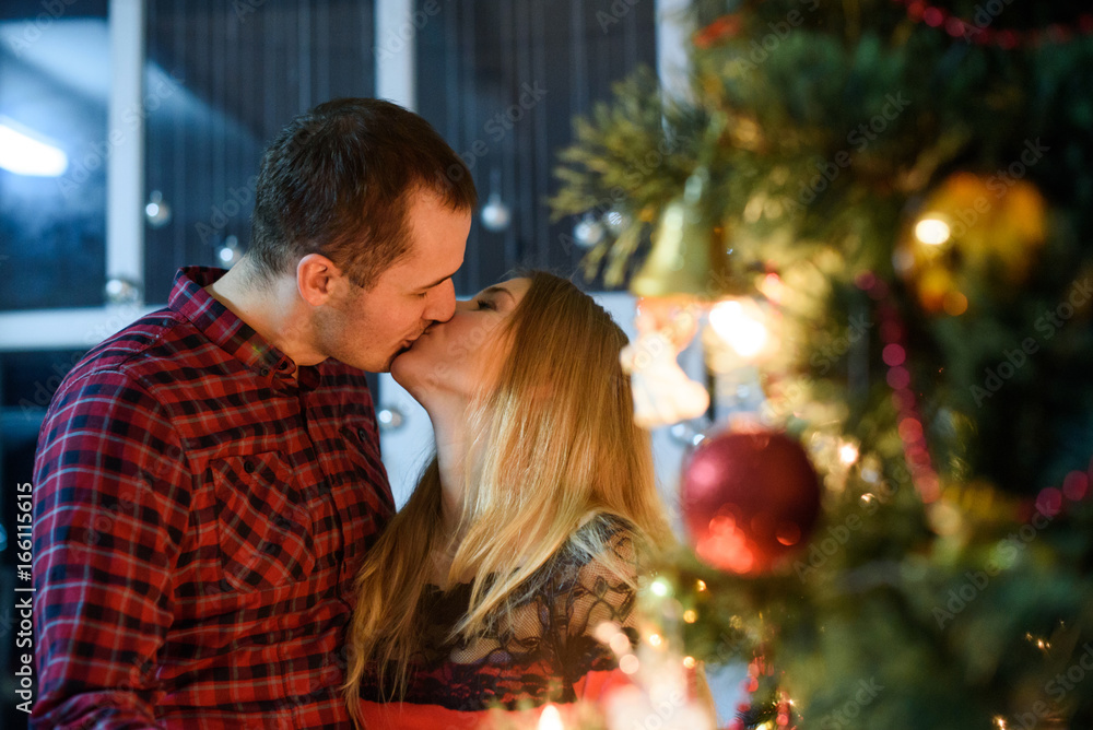 Attractive couple on Christmas day standing in front of the decorated tree and kissing Attractive couple on Christmas day standing in front of the decorated tree and kissing