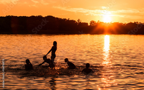 Kids and families are having fun at a lake under sunset