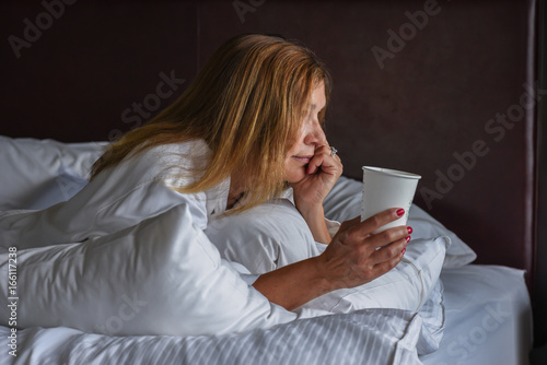 Woman in luxury hotel room laying on bed with cup of coffee in Toronto, Canada