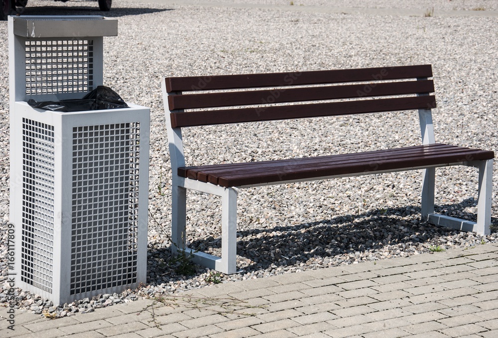a modern bench and trash can on gravel sidewalk
