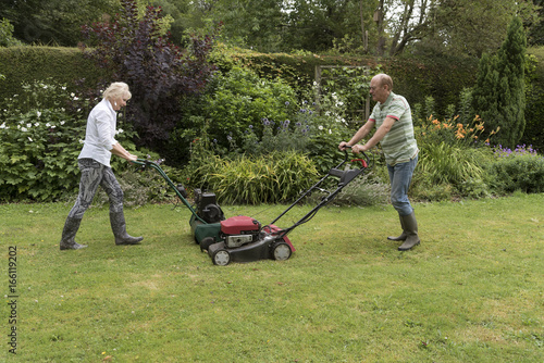 Man and woman with lawn mowers working in a country garden