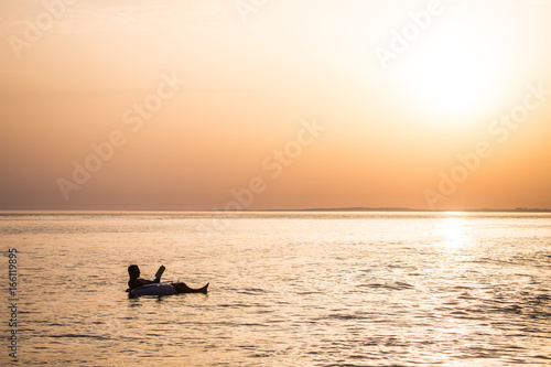Young man in relax in the ocean water on inflatable ring on sunset read a book.
