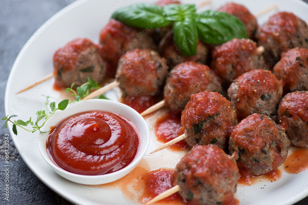 Close-up of oven-baked meatballs on skewers served with tomato sauce, selective focus