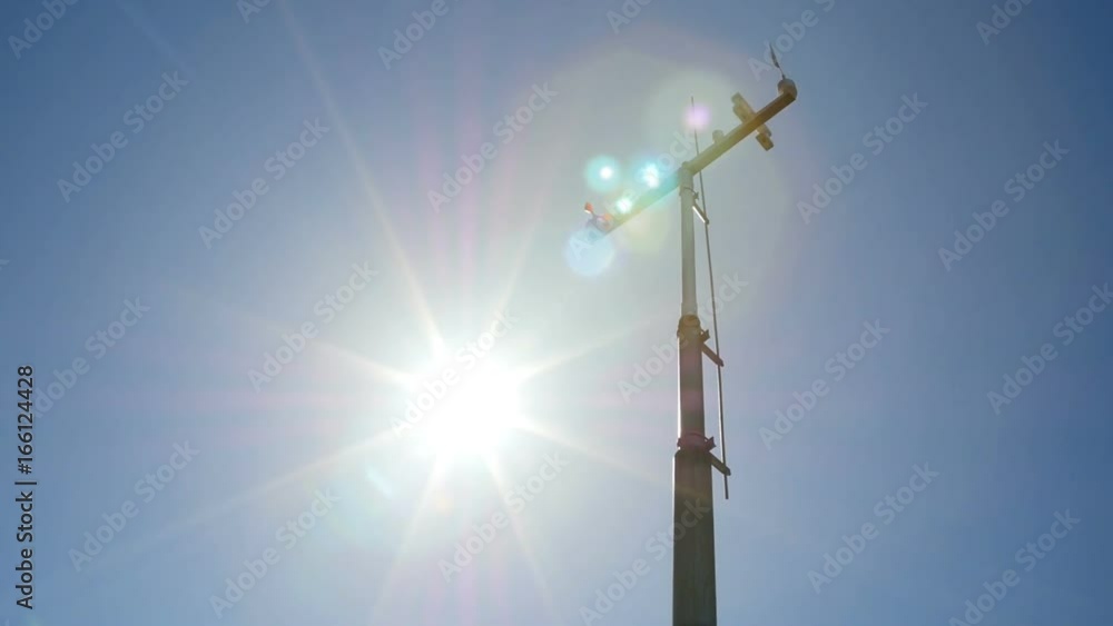 The anemometer in the sun's rays measures the wind speed. The meteo station on the blue sky background. The anemometer in the sun's rays measures the wind speed. The meteo station on the blue sky background.