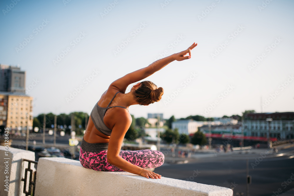 Young woman in yoga pose, city on background