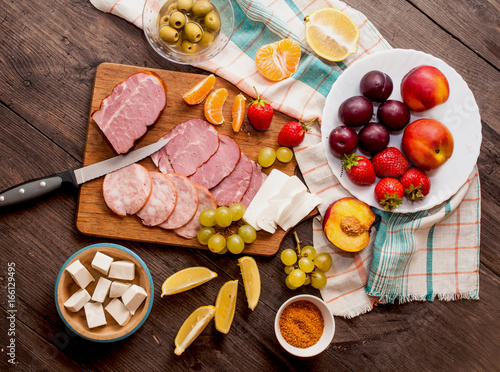 A set of meat delicacies, cheese and fruits on a dark, wooden background. Top view, banner for a cafe.