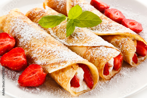 Crepes with strawberries and cream on white background