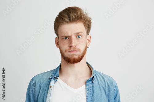 Portrait of nervous young man with beard looking at camera raising up brow over white background.