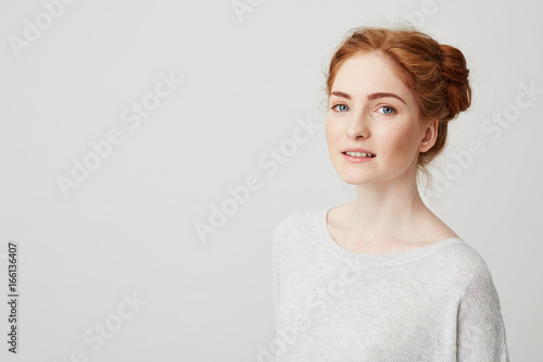 Portrait of beautiful redhead girl with buns and freckles smiling looking at camera over white background.