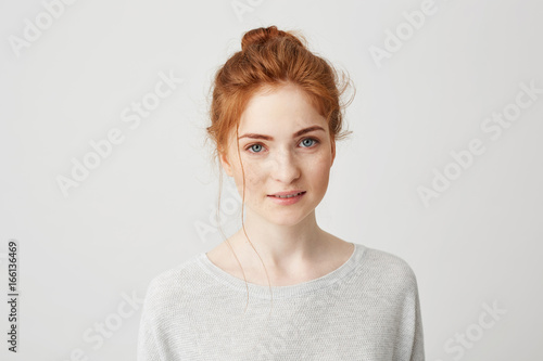 Portrait of happy tender ginger girl with blue eyes and freckles looking at camera smiling over white background.