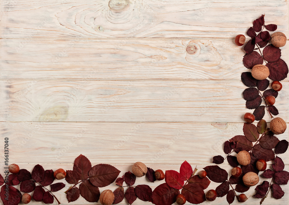 Flat lay frame of autumn crimson leaves, hazelnuts and walnuts on a light wooden background. Flat lay frame of autumn crimson leaves, hazelnuts and walnuts on a light wooden background.