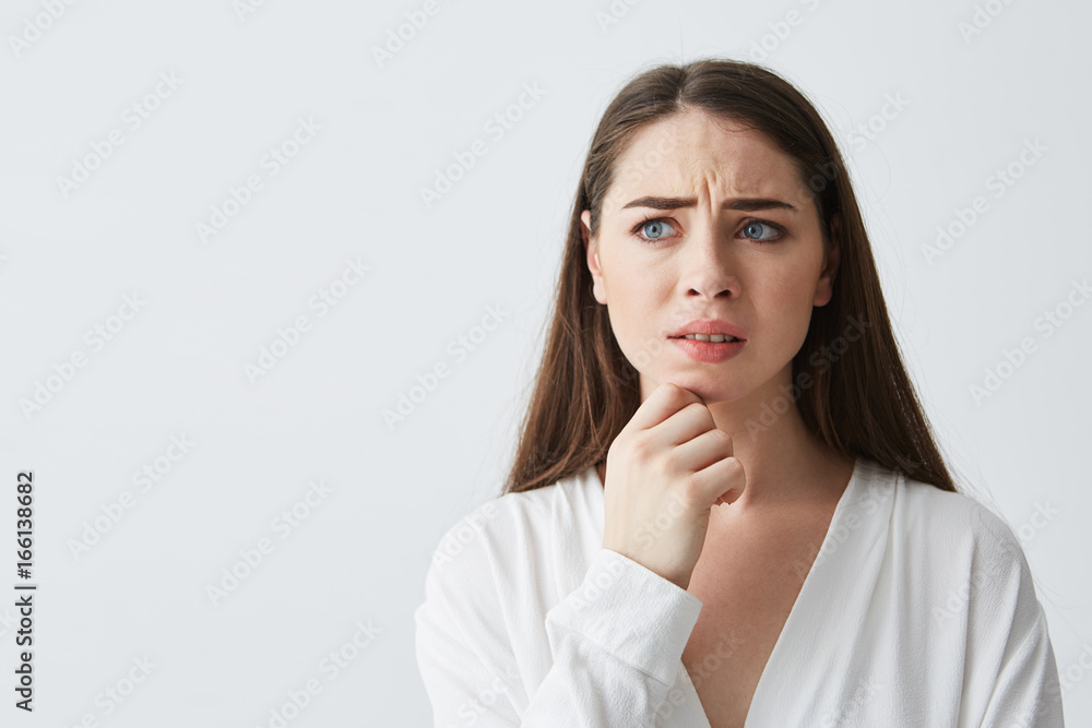 Portrait of nervous young brunette girl thinking looking in side holding hand on chin over white background. Portrait of nervous young brunette girl thinking looking in side holding hand on chin over white background.