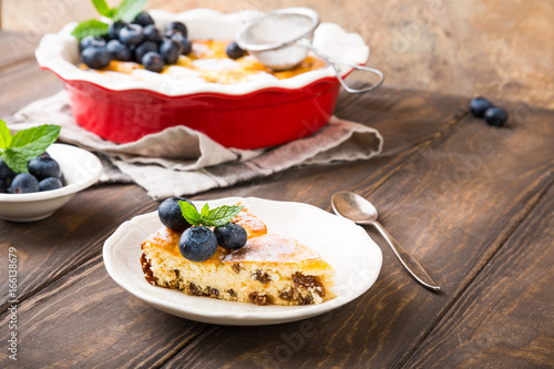 Piece of homemade cheesecake made from cottage cheese, decorated with blueberries and mint on wooden background. Healthy food concept with copy space.