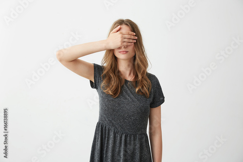 Young pretty girl covering closing eyes behind hand over white background.