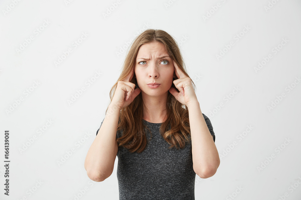 Young beautiful girl thinking with fingers on temples looking up over white background. Young beautiful girl thinking with fingers on temples looking up over white background.