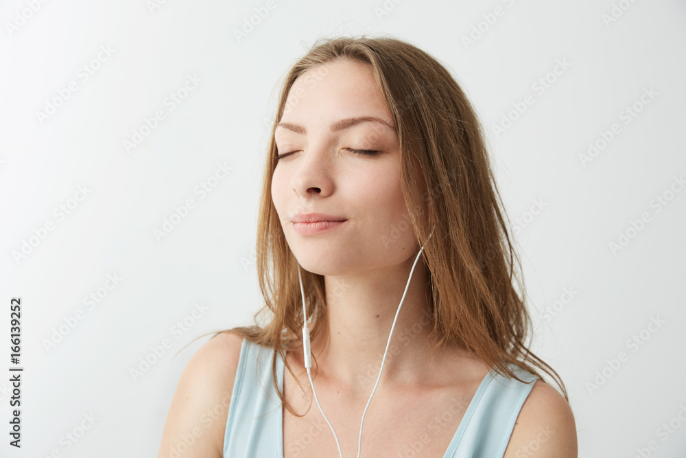 Tender young pretty girl smiling with closed eyes listening to streaming music in headphones over white background. Tender young pretty girl smiling with closed eyes listening to streaming music in headphones over white background.