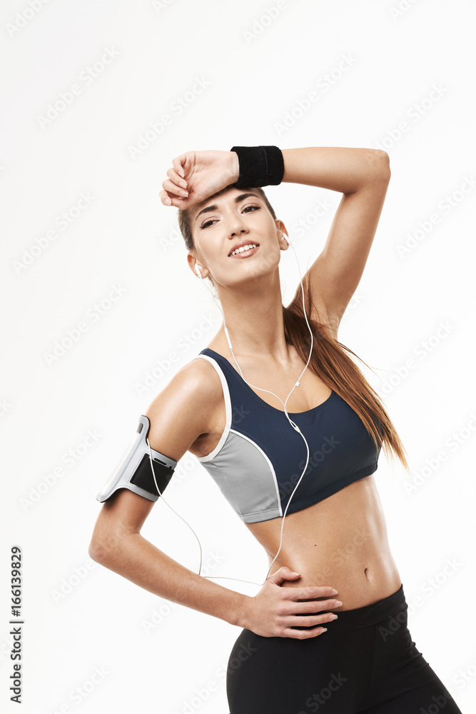 Fototapeta premium Tired sporty girl in headphones looking in side holding hand on forehead over white background.