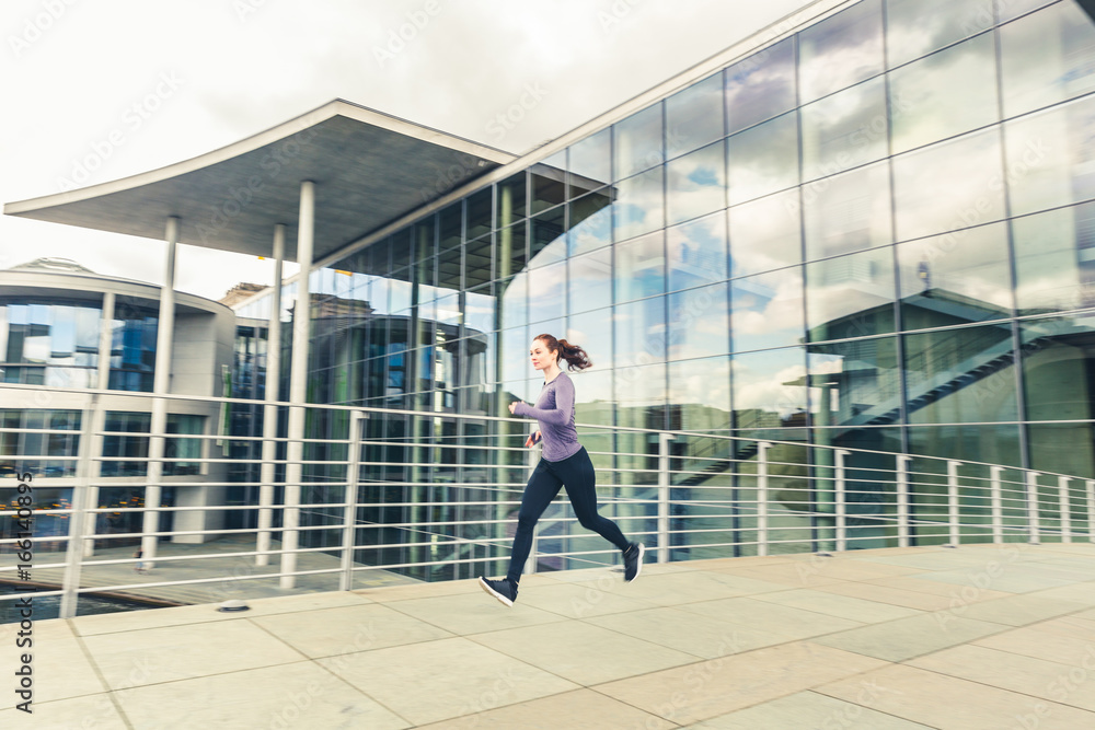 Woman jogging, panning view with modern buildings on background Woman jogging, panning view with modern buildings on background