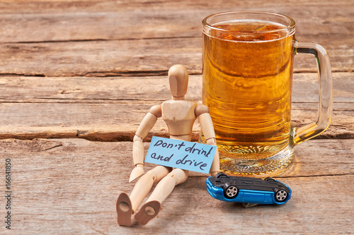 Do not drink and drive concept. Human wooden dummy sitting with beer, car, old wooden background. photo