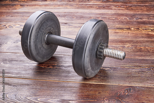 Single black dumbblle isolated. Heavy dumbbell for weightlifting on wooden background.