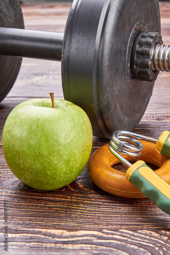 Sport activity and healthy lifestyle. Vertical image of dumbbells, green apple, expanders on wooden floor.