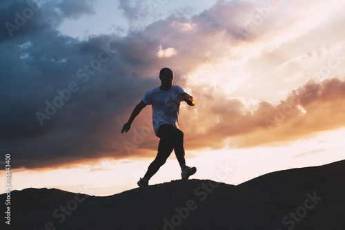 Muscular athlete is engaged in fitness and jogging on nature. Jogging on outdoor at background of sunset