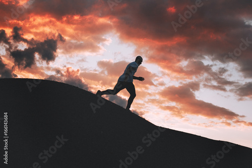 Silhouette of a fast running man on an uneven trail outdoors at sunset
