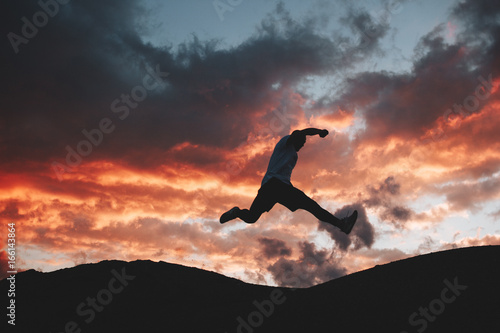 Male athlete engaged in parkour and freeran in the background of a beautiful sunset. Silhouette of a man at the moment of a jump