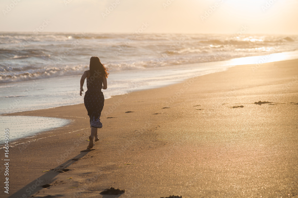 girl in a dress runs through the sandy beach along the stormy sea at sunset girl in a dress runs through the sandy beach along the stormy sea at sunset