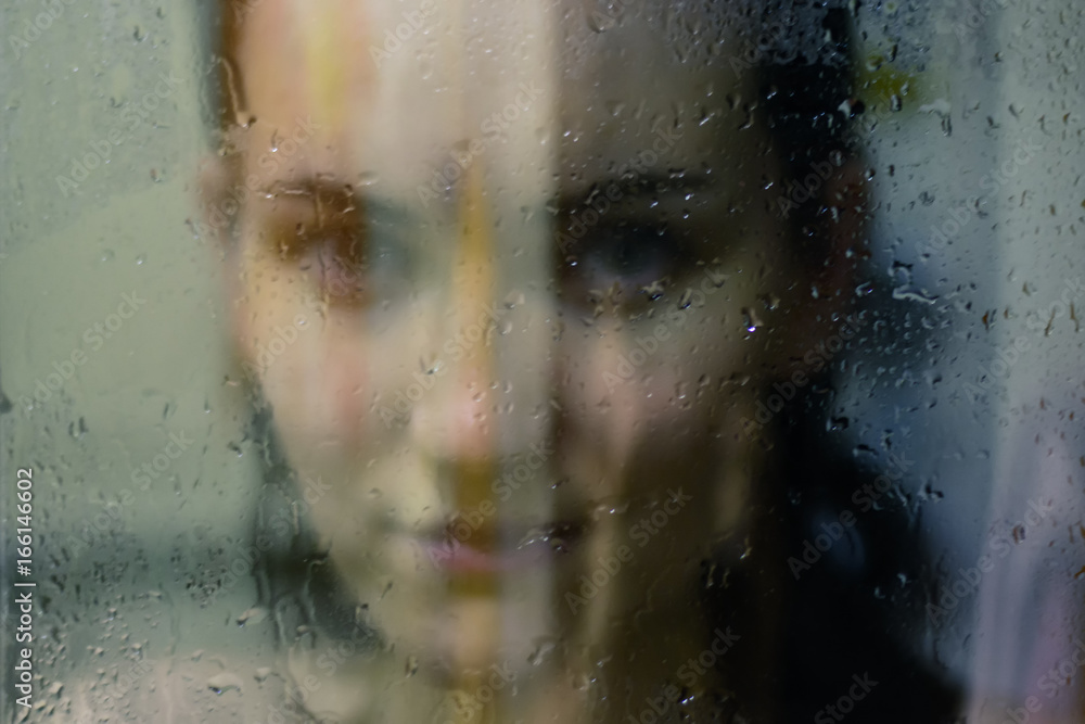 Beautiful woman behind the glass with water drops looking directly at camera. Girl takes a shower, voyeurism