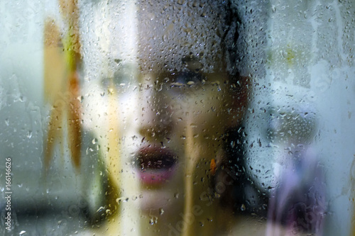 Obraz na plátne Beautiful woman behind the glass with water drops looking directly at camera