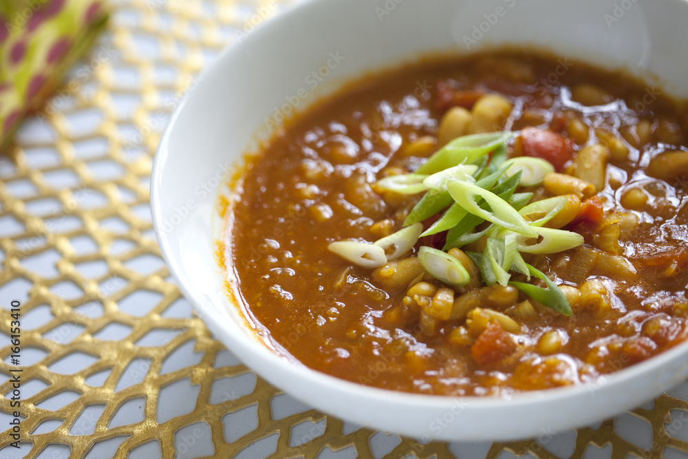 Bean and tomato soup with green onions on gold placemat Bean and tomato soup with green onions on gold placemat