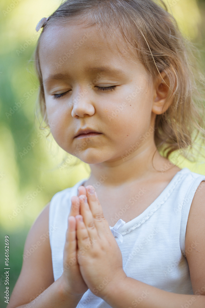 Cute little girl 4 - 5 years old meditating at green summer park in lotus pose Cute little girl 4 - 5 years old meditating at green summer park in lotus pose