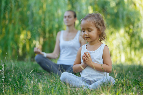 Young mother and cute little daughter meditating in lotus pose together