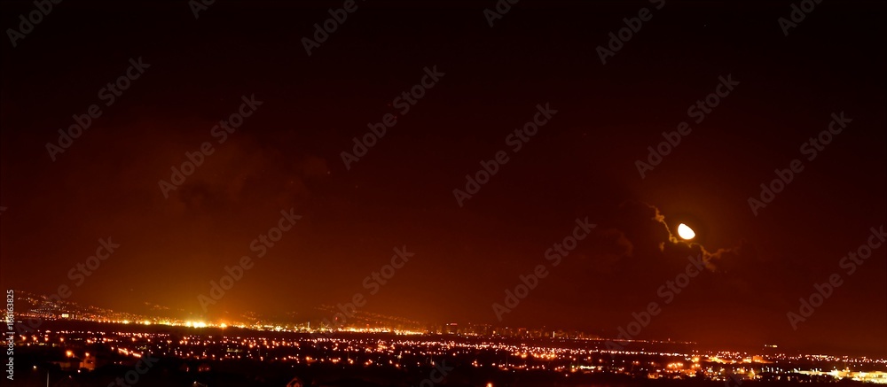 Moon Over Hawaii / Moon partially covered with clouds shines down over the city in Hawaii.