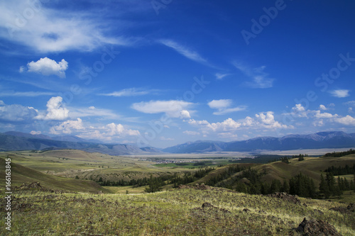 Cloud over the mountain range. Blue sky and green grass in a valley